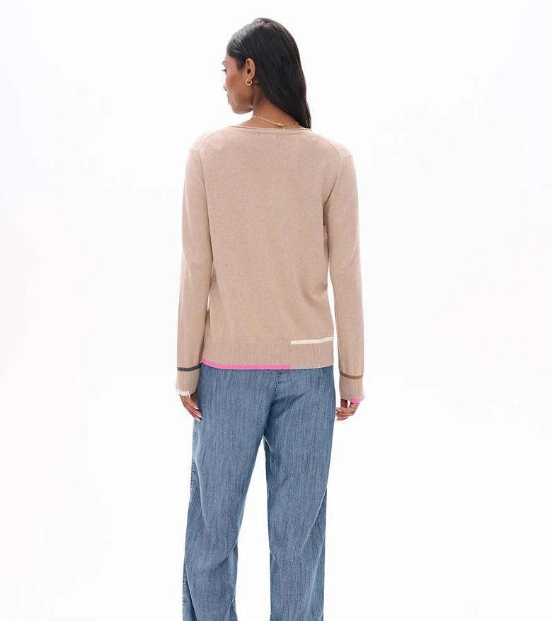 A woman viewed from behind wearing a beige knit sweater with contrasting dark cuffs and a pink hem, paired with wide-leg blue jeans, against a plain white studio background.