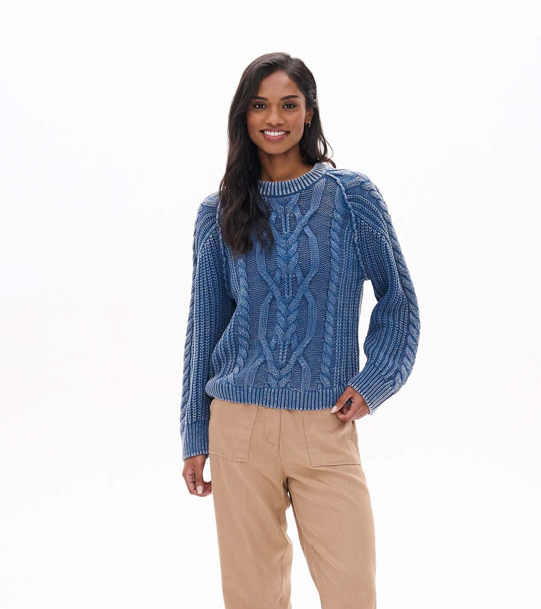 Woman wearing a blue cable knit sweater, beige pants, and brown boots on a white background