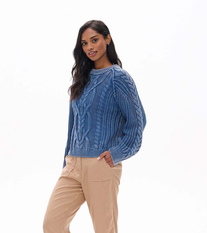 Woman wearing a blue sweater, beige pants, and brown boots on a white background