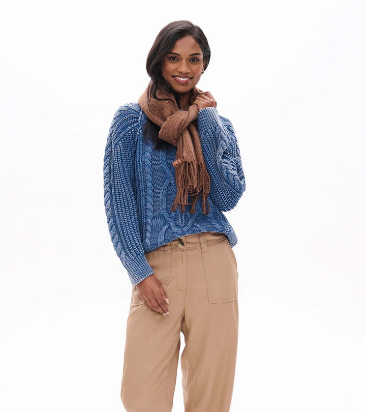 Woman wearing a blue sweater, beige pants, and brown boots on a white background