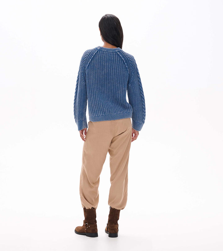 Person wearing a blue checkered sweater and beige pants on a white background