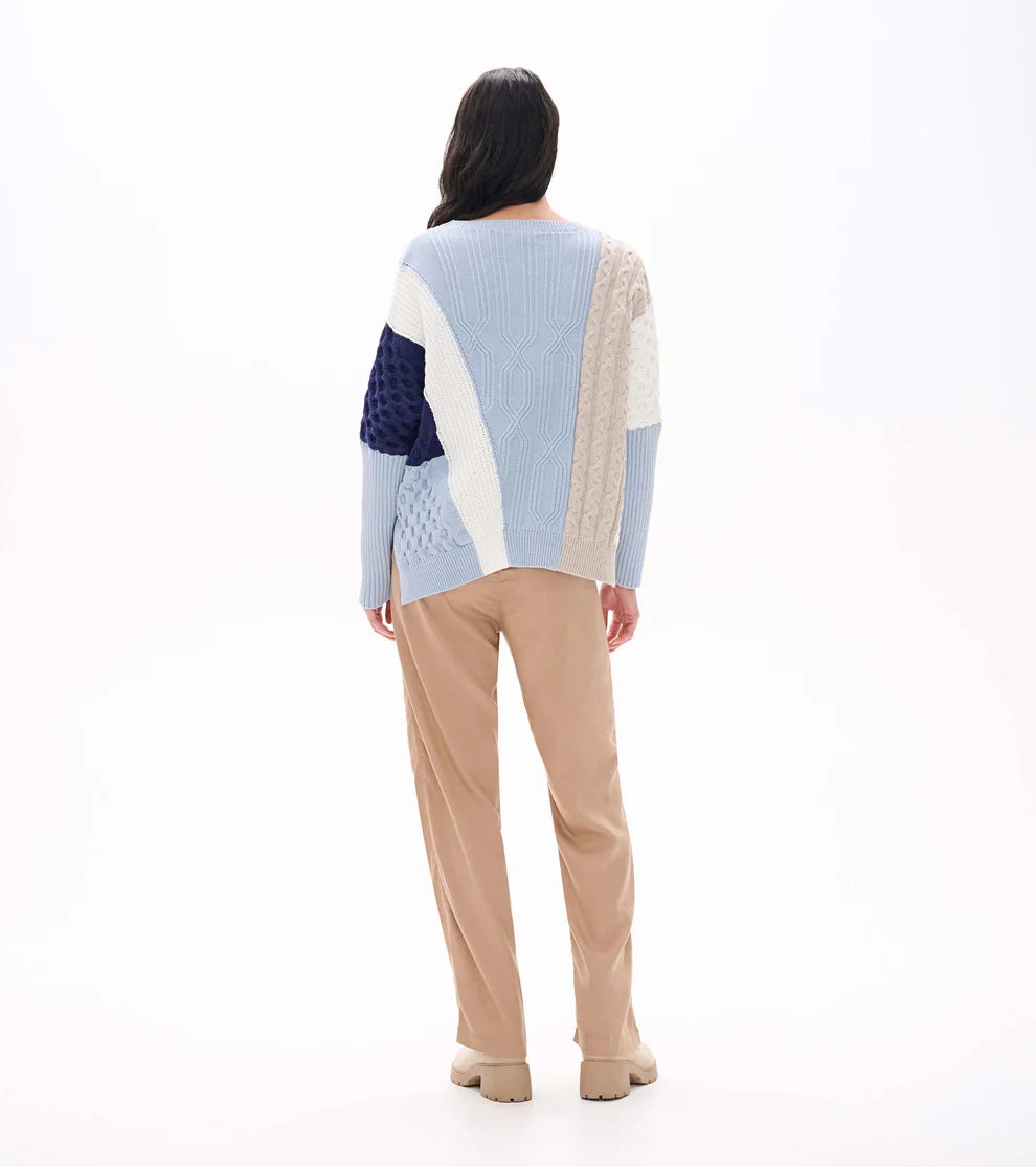 Person wearing a light blue and beige patterned sweater with beige pants on a white background