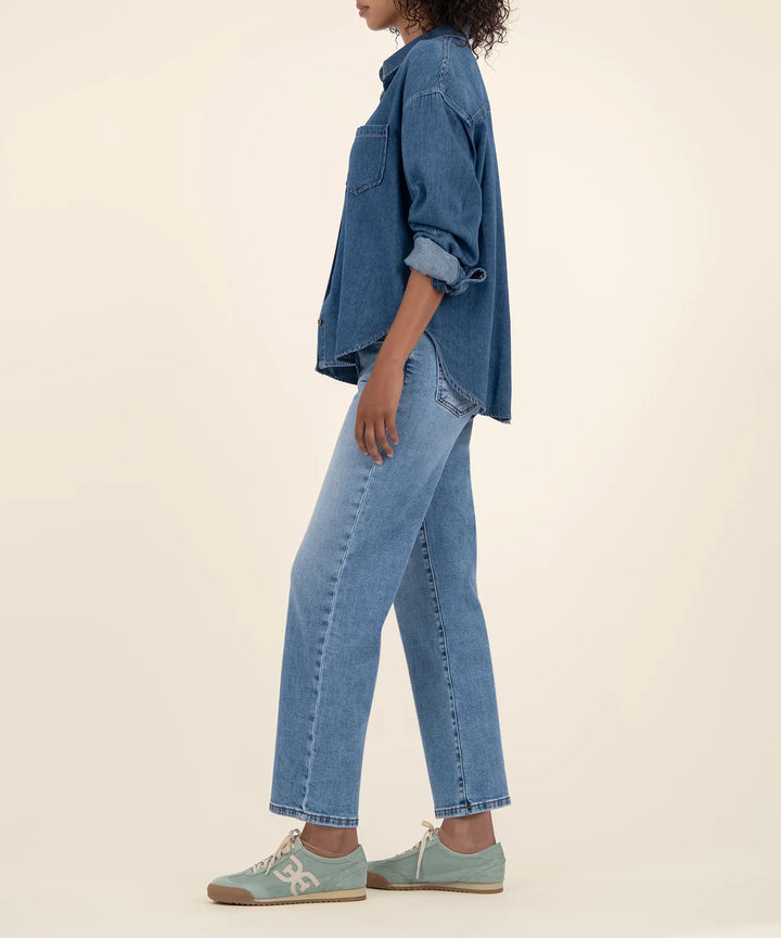 Person wearing a blue denim shirt and jeans on a beige background