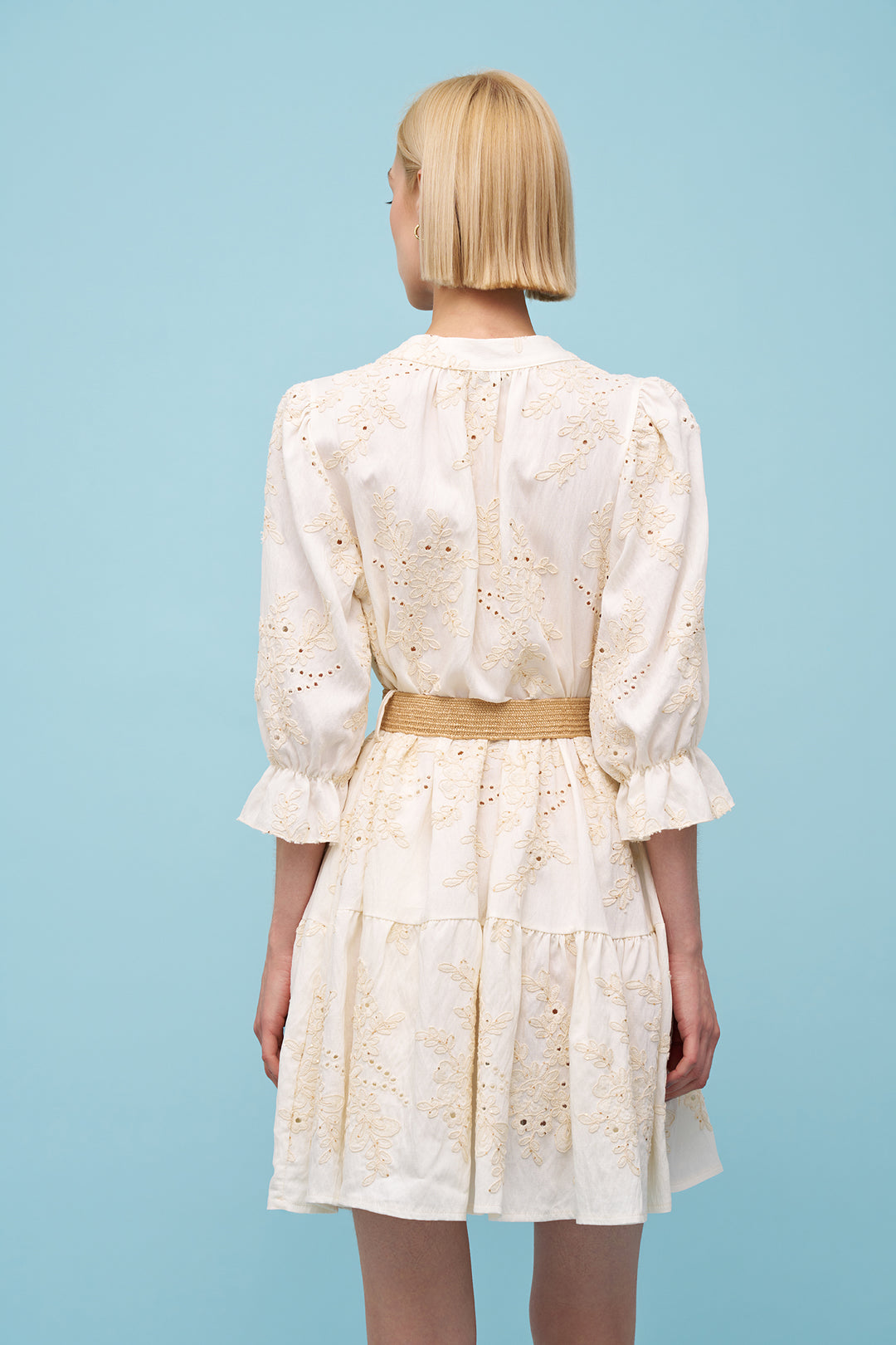 Woman wearing a white floral dress with a belt against a light blue background