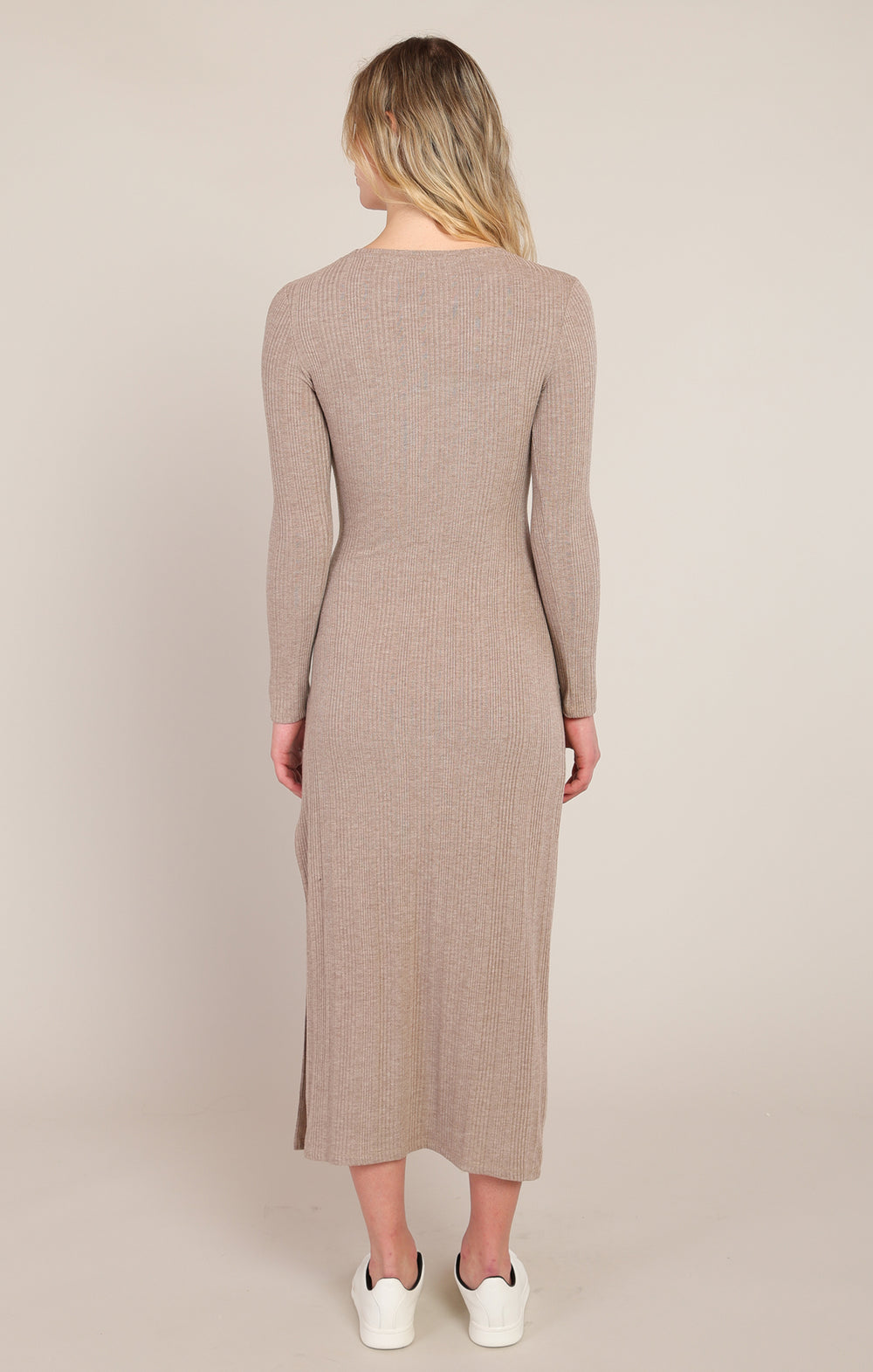 Woman wearing a long-sleeve, knee-length dress in a neutral color on a plain background