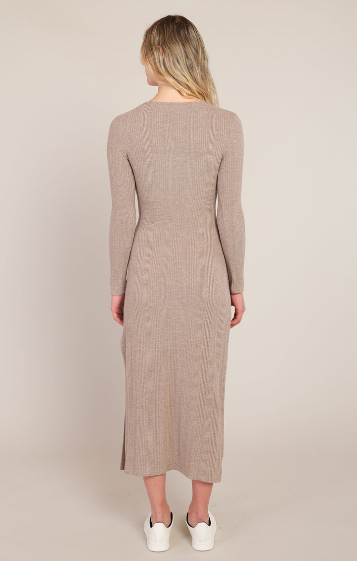 Woman wearing a long-sleeve, knee-length dress in a neutral color on a plain background