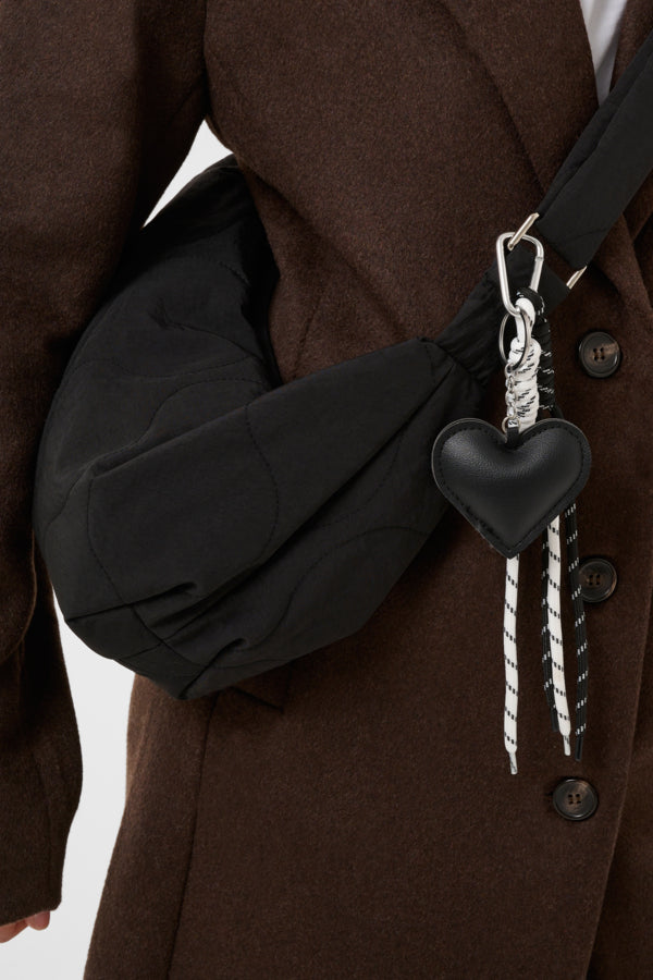 Person wearing a brown coat with a black bag featuring a heart-shaped charm.