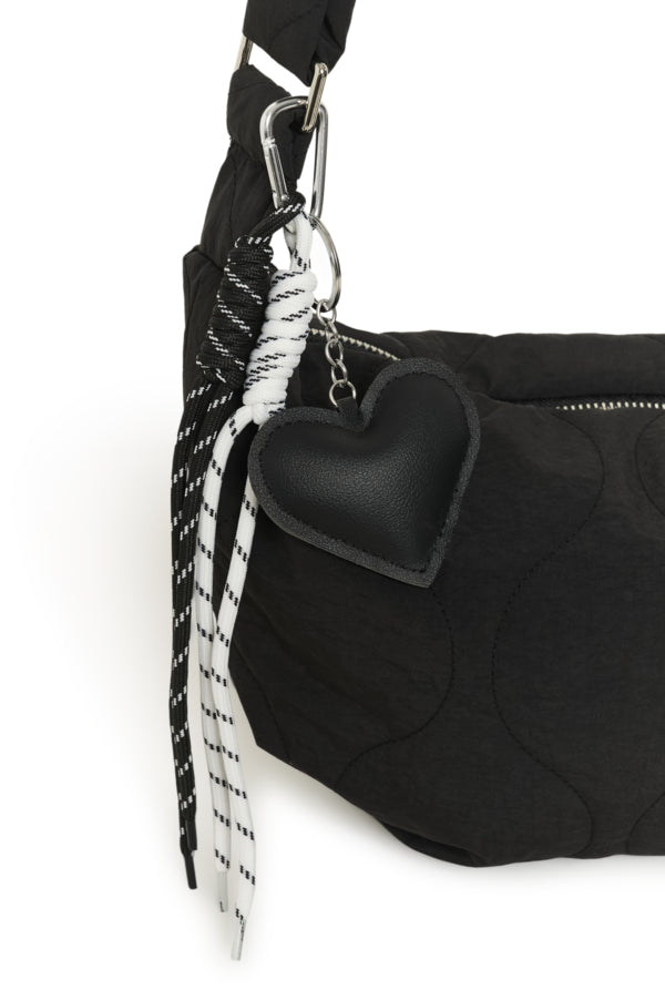 Black bag with a heart-shaped black object attached to a strap on a white background