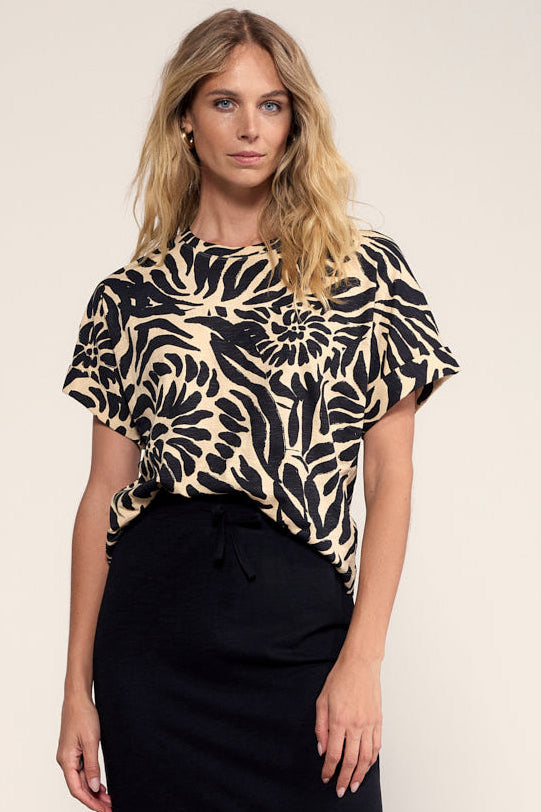 Woman wearing a black and beige patterned top with a plain background