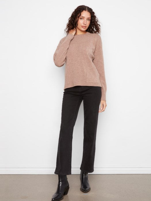 A woman modeling a dusty rose knit sweater and black wide-leg pants against a white wall.