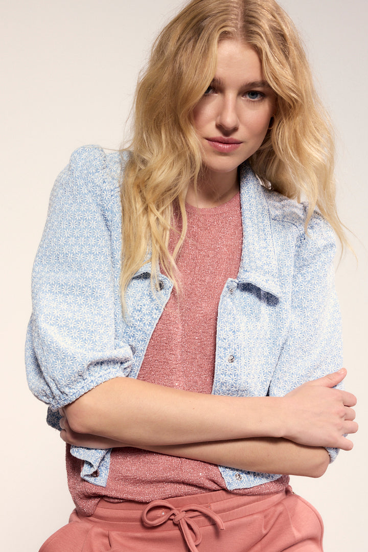 Woman wearing a light blue jacket over a pink top and pants on a beige background