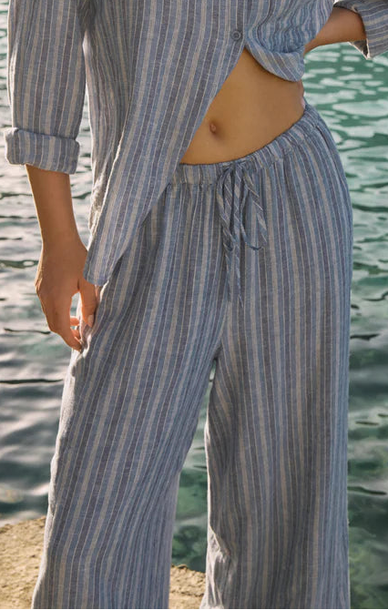 Woman in a striped outfit standing by a body of water with mountains in the background