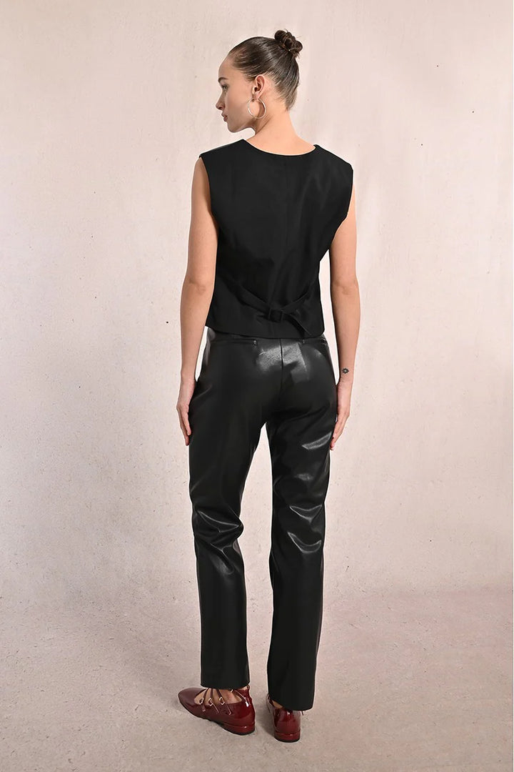 Person wearing a black sleeveless top and black leather pants on a neutral background