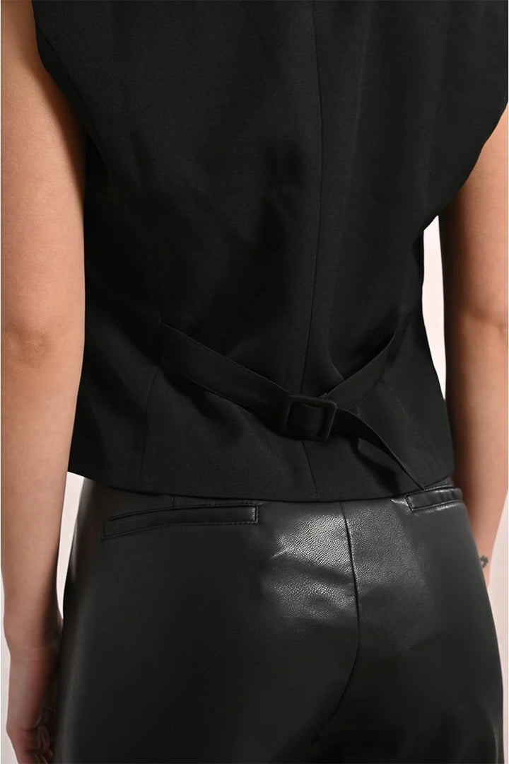 Black sleeveless top with a belt and black leather pants on a neutral background