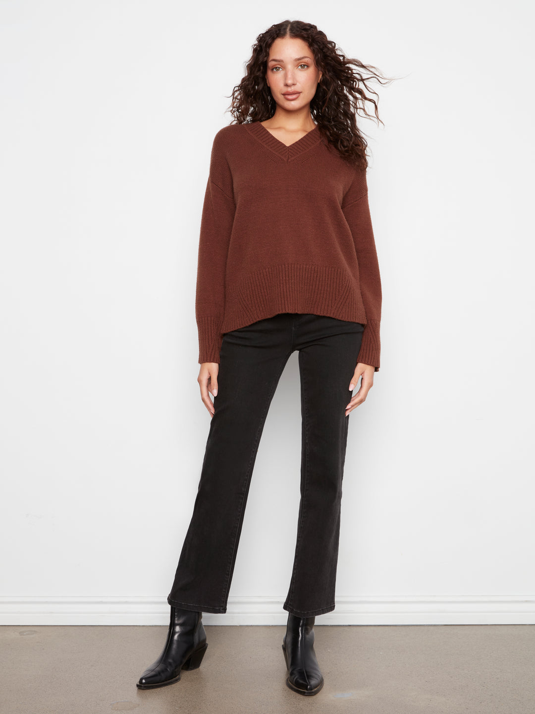 Woman wearing a brown sweater and black pants against a white background