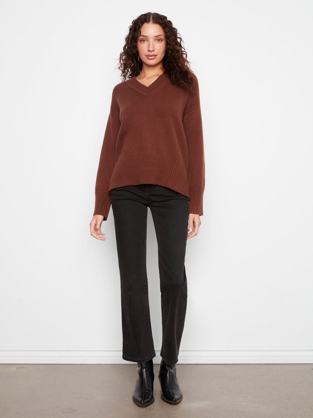 Woman wearing a brown sweater and black pants against a white background