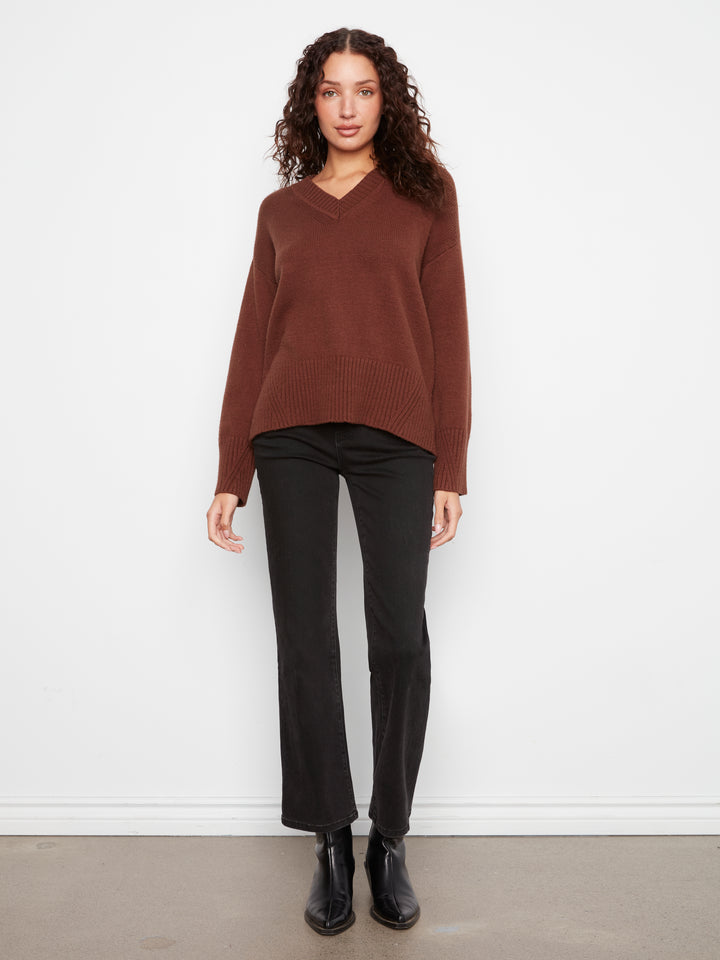 Woman wearing a brown sweater and black pants against a white background