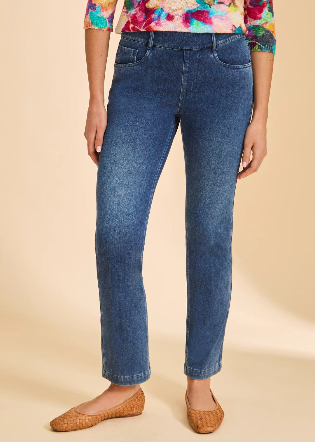 Person wearing blue jeans and a colorful floral top on a beige background