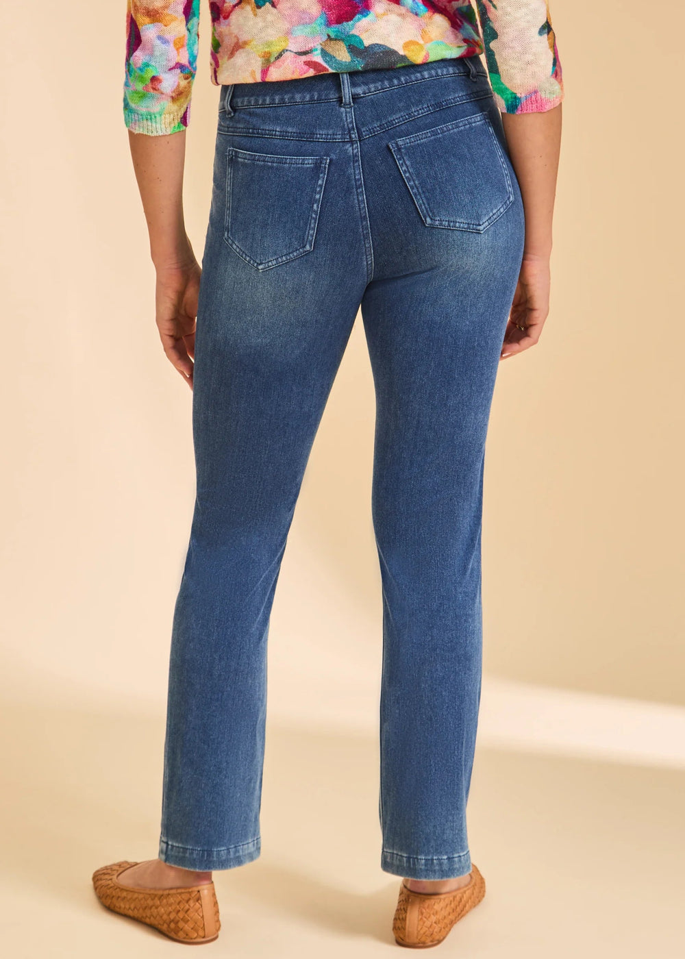Person wearing blue jeans and a colorful top on a beige background