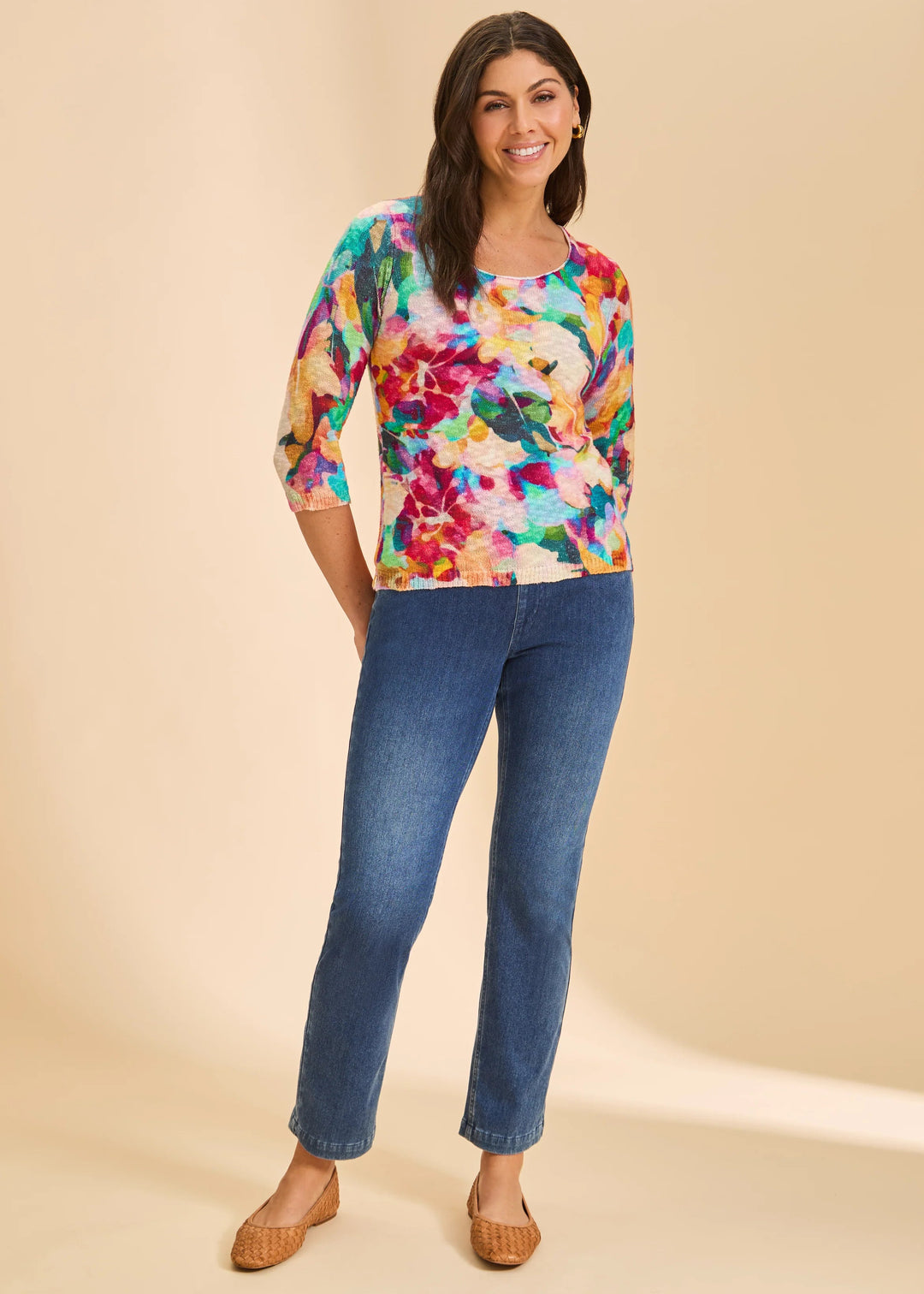Woman wearing a colorful floral top and blue jeans on a beige background
