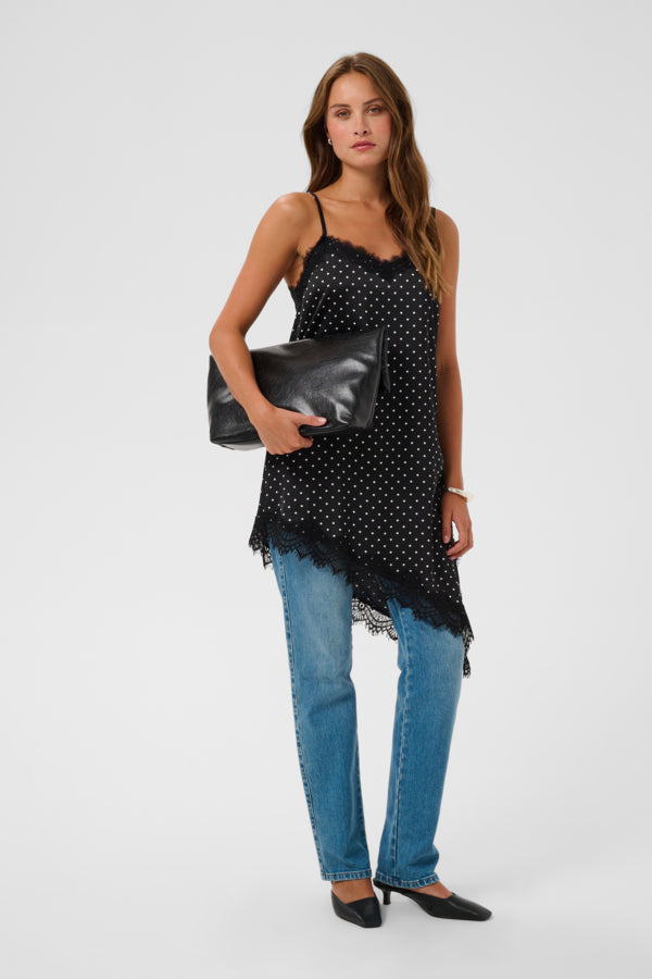 A woman modeling a black camisole top with white polka dots and a lace hem, paired with blue jeans, black heels, and holding a black clutch bag against a light gray studio background.