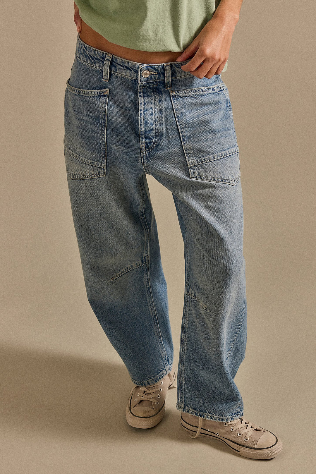Person wearing blue jeans and beige sneakers on a beige background