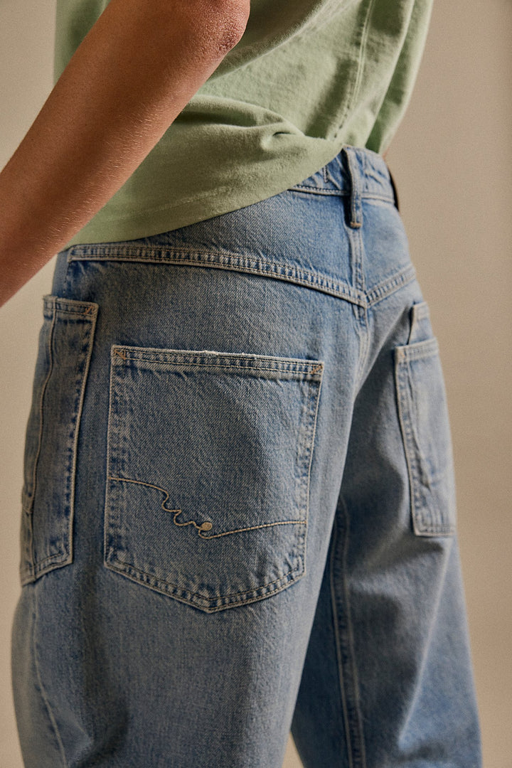 Person wearing a green shirt and blue jeans with a visible brand logo on a beige background