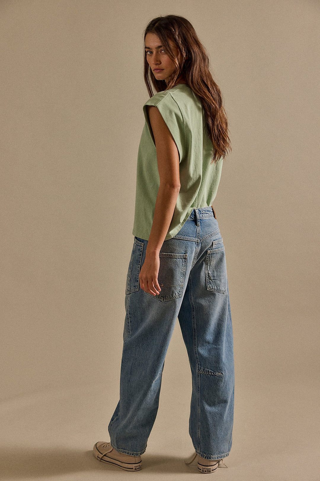 Woman wearing a light green sleeveless top and blue jeans against a beige background