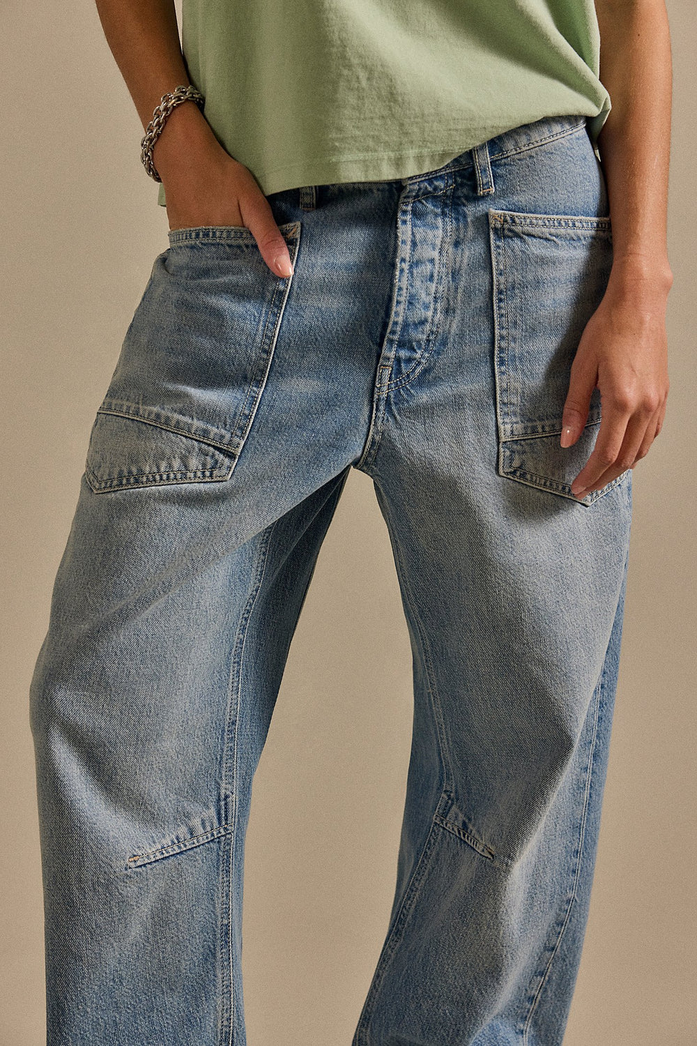 Person wearing light blue jeans and a green top on a beige background