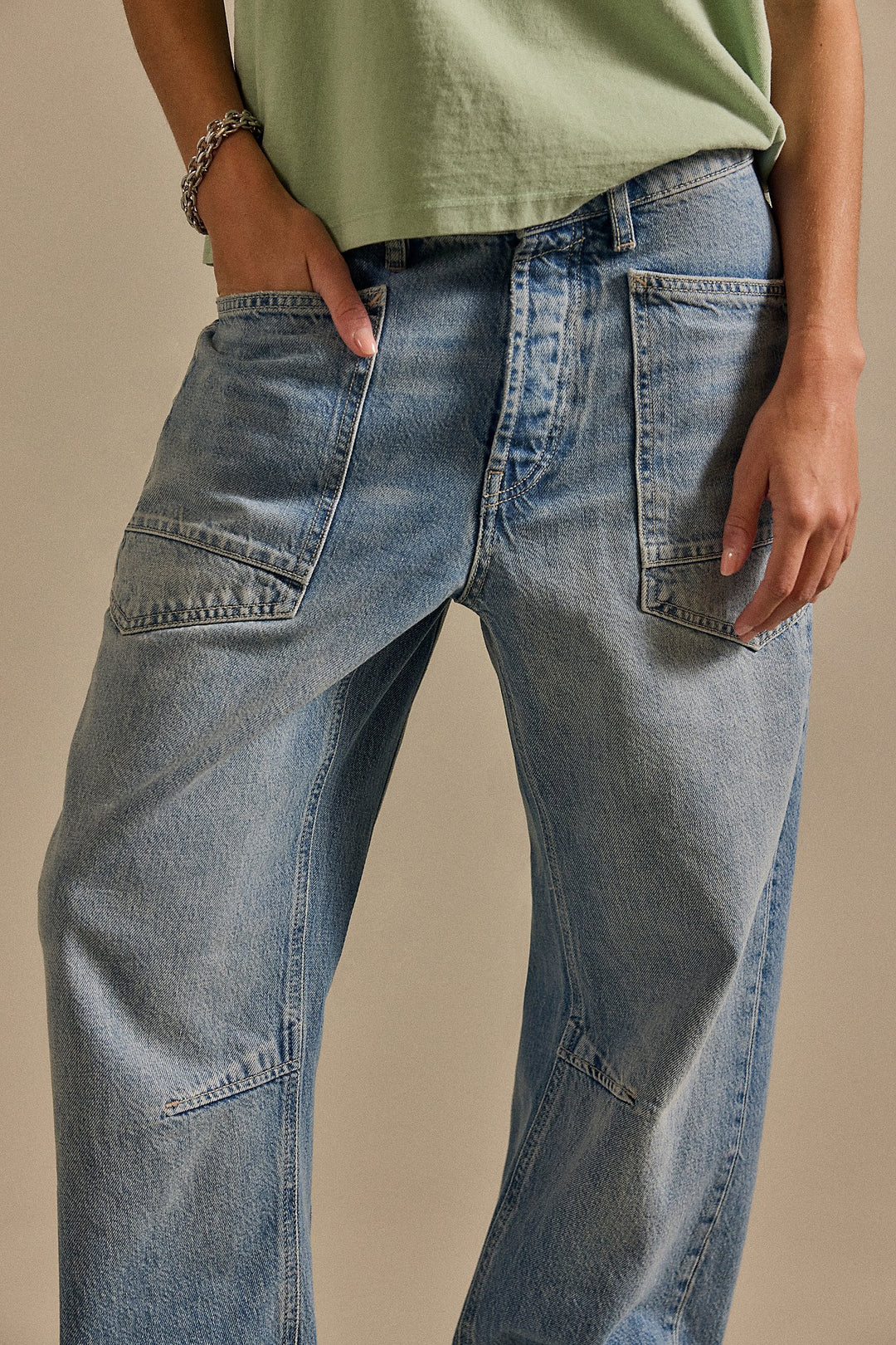Person wearing light blue jeans and a green top on a beige background