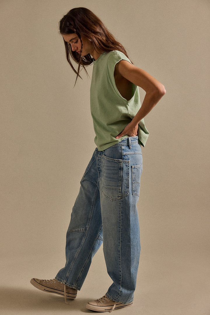 Woman wearing a green sleeveless top and blue jeans against a beige background