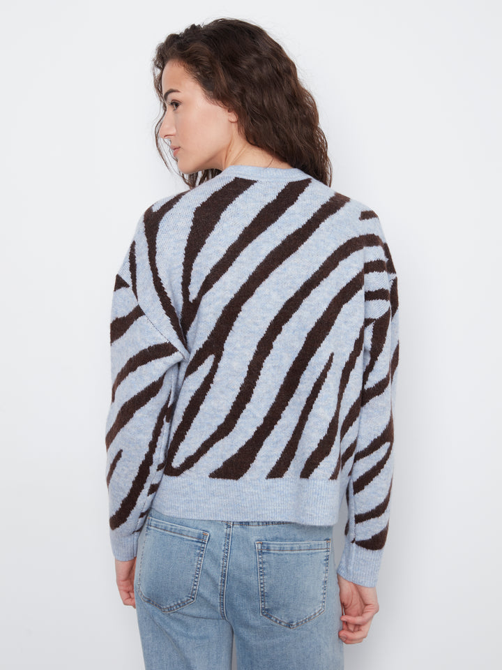 A woman shown from the back wearing a light gray and dark brown zebra-striped knit sweater with light blue jeans, set against a plain white studio background.