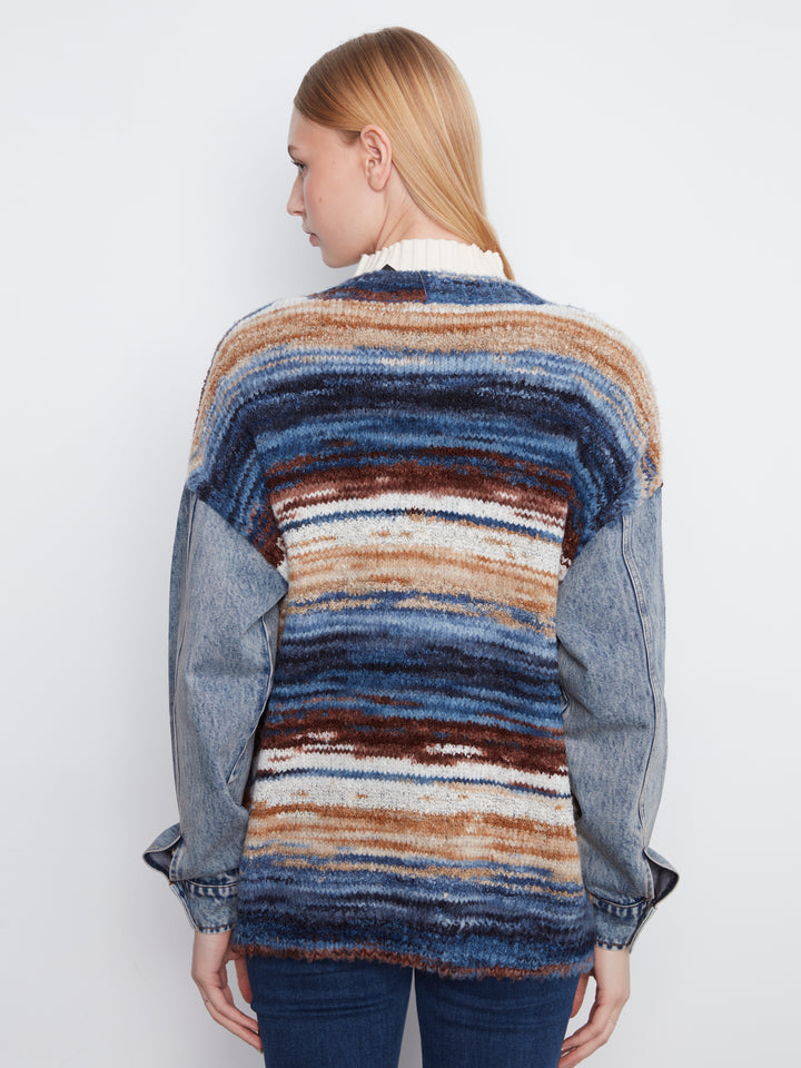 Person wearing a multicolored striped sweater over a denim jacket on a plain background