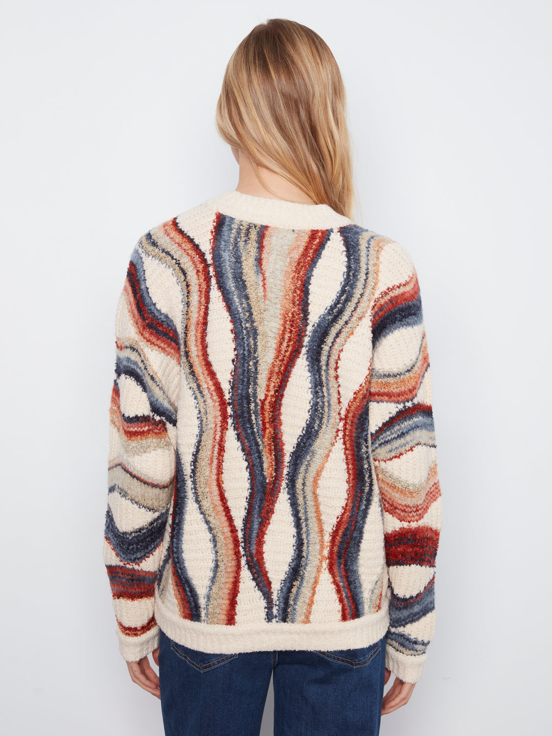 A woman viewed from the back wearing a textured sherpa-style cardigan with wavy vertical stripes in cream, rust red, navy blue, and gray, paired with dark blue jeans against a plain white background.