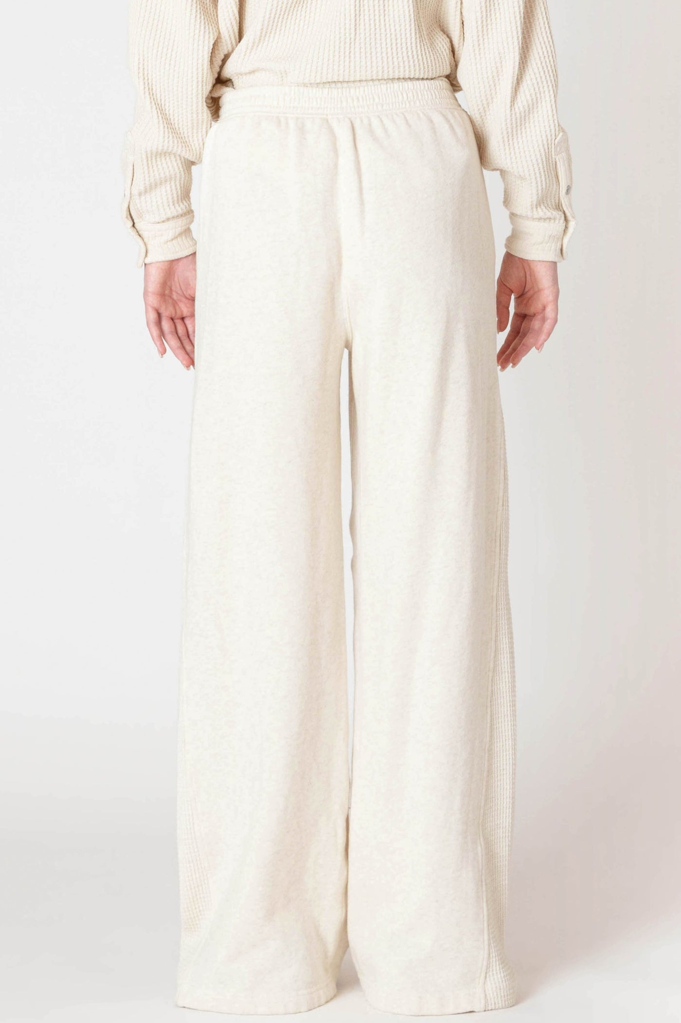 Person wearing a cream sweater and wide-leg pants on a white background