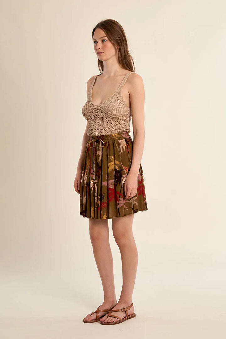 Woman wearing a beige top and patterned skirt on a plain background