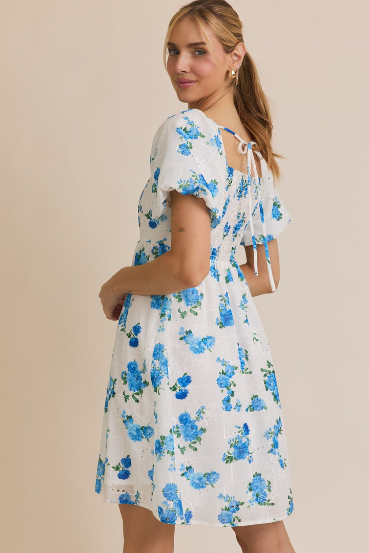 Woman wearing a white dress with blue floral pattern against a beige background