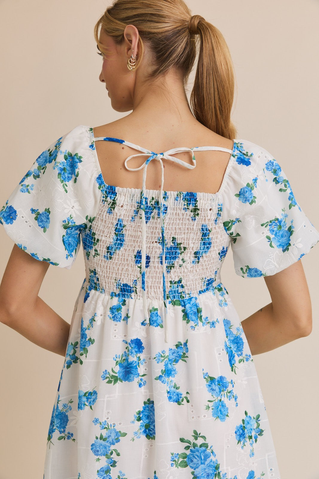 Woman wearing a white dress with blue floral pattern on a beige background