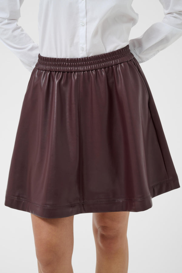 A dark brown faux-leather A-line mini skirt with an elastic waistband, shown on a model wearing a white button-down shirt against a light gray background.
