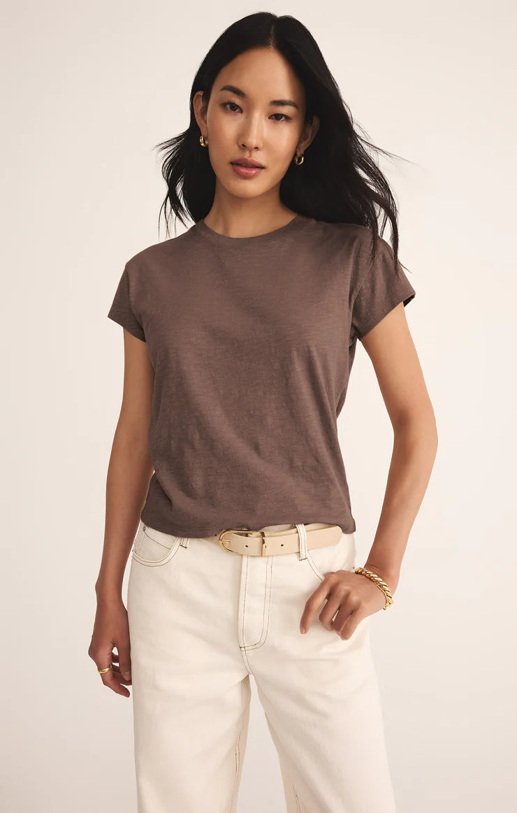 Woman wearing a brown t-shirt and white pants against a plain background