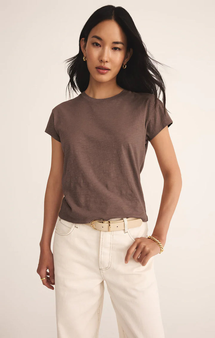 Woman wearing a brown t-shirt and white pants against a plain background