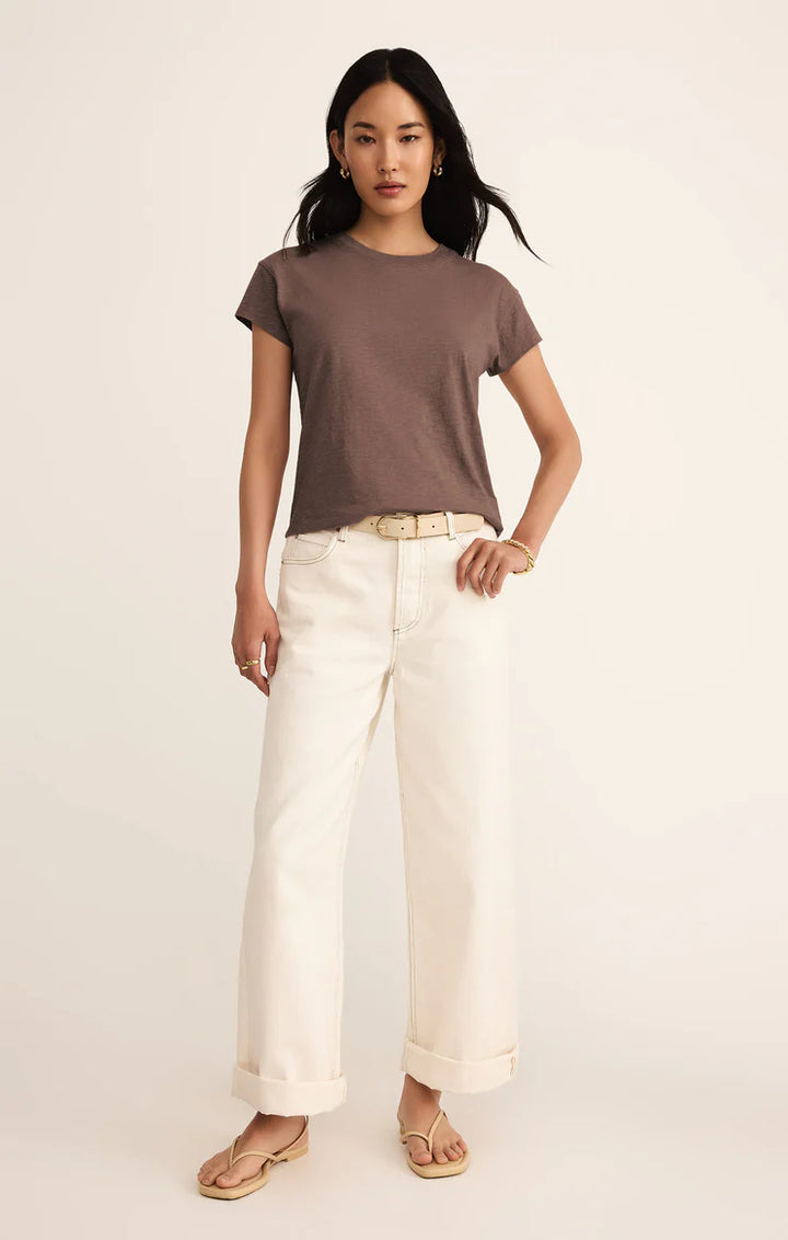 Woman wearing a brown t-shirt and white pants on a beige background