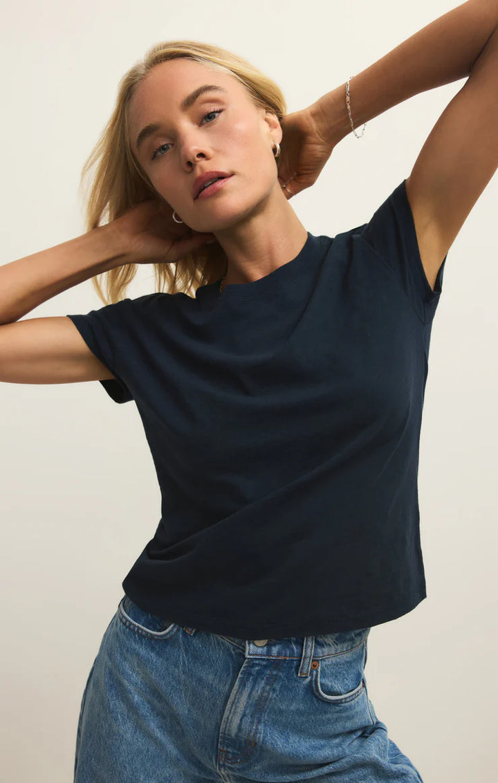 Woman wearing a navy blue t-shirt and blue jeans against a plain background