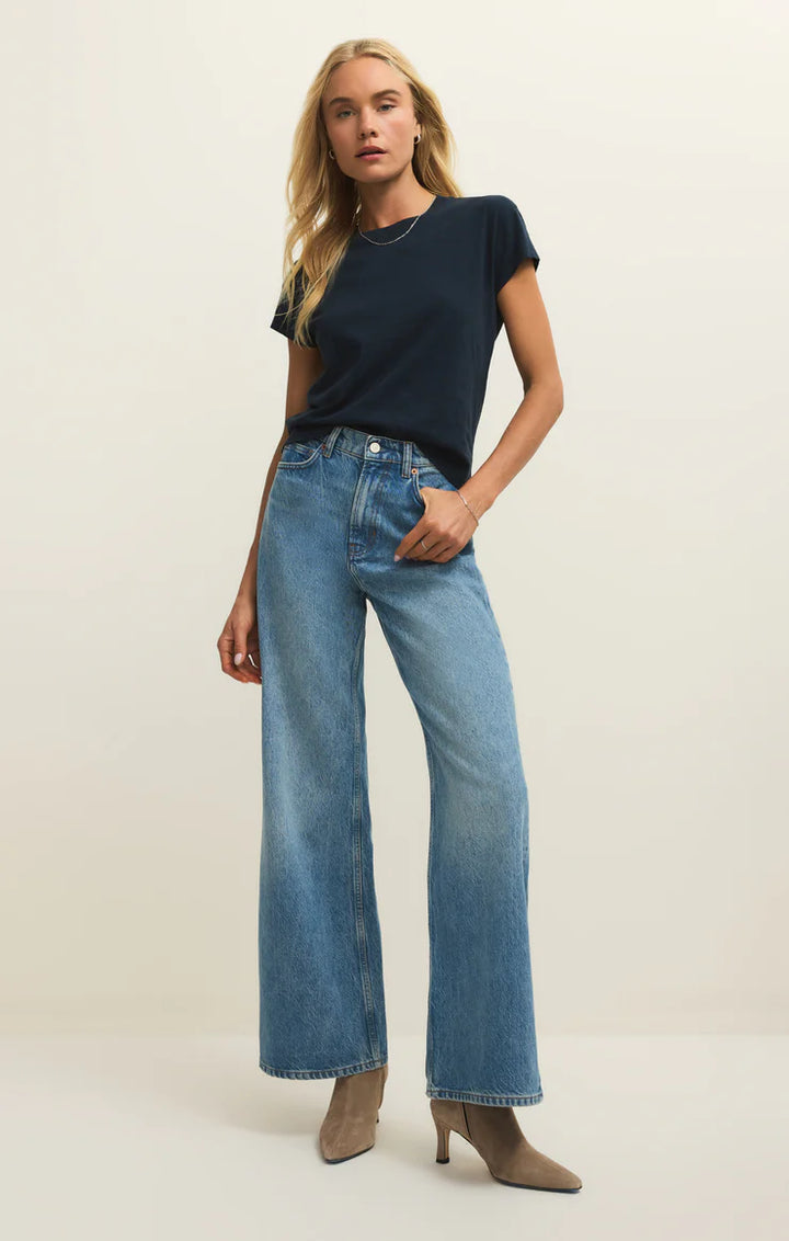Woman wearing a navy t-shirt and blue jeans on a plain background