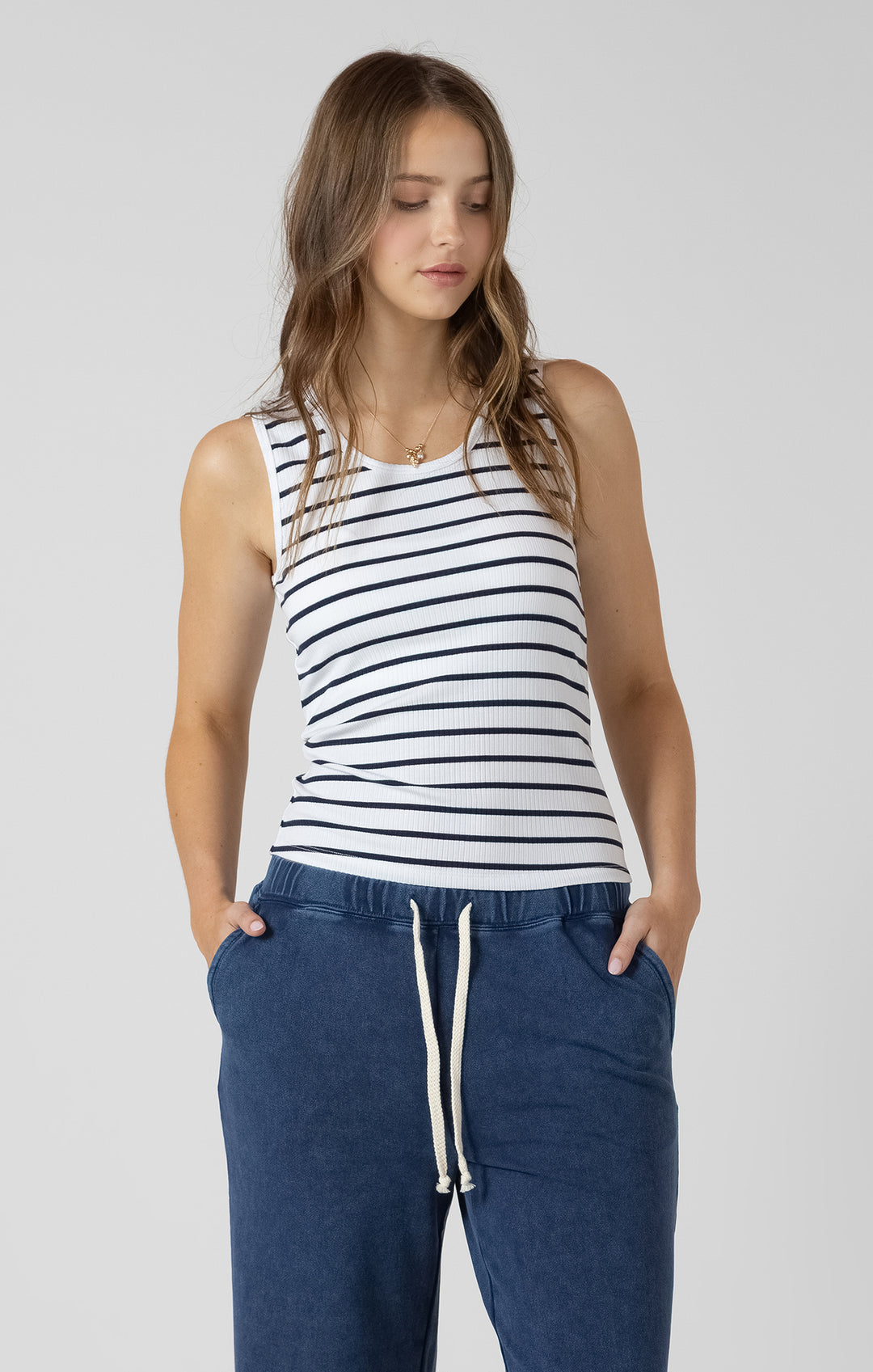 Woman wearing a striped tank top and blue pants on a plain background