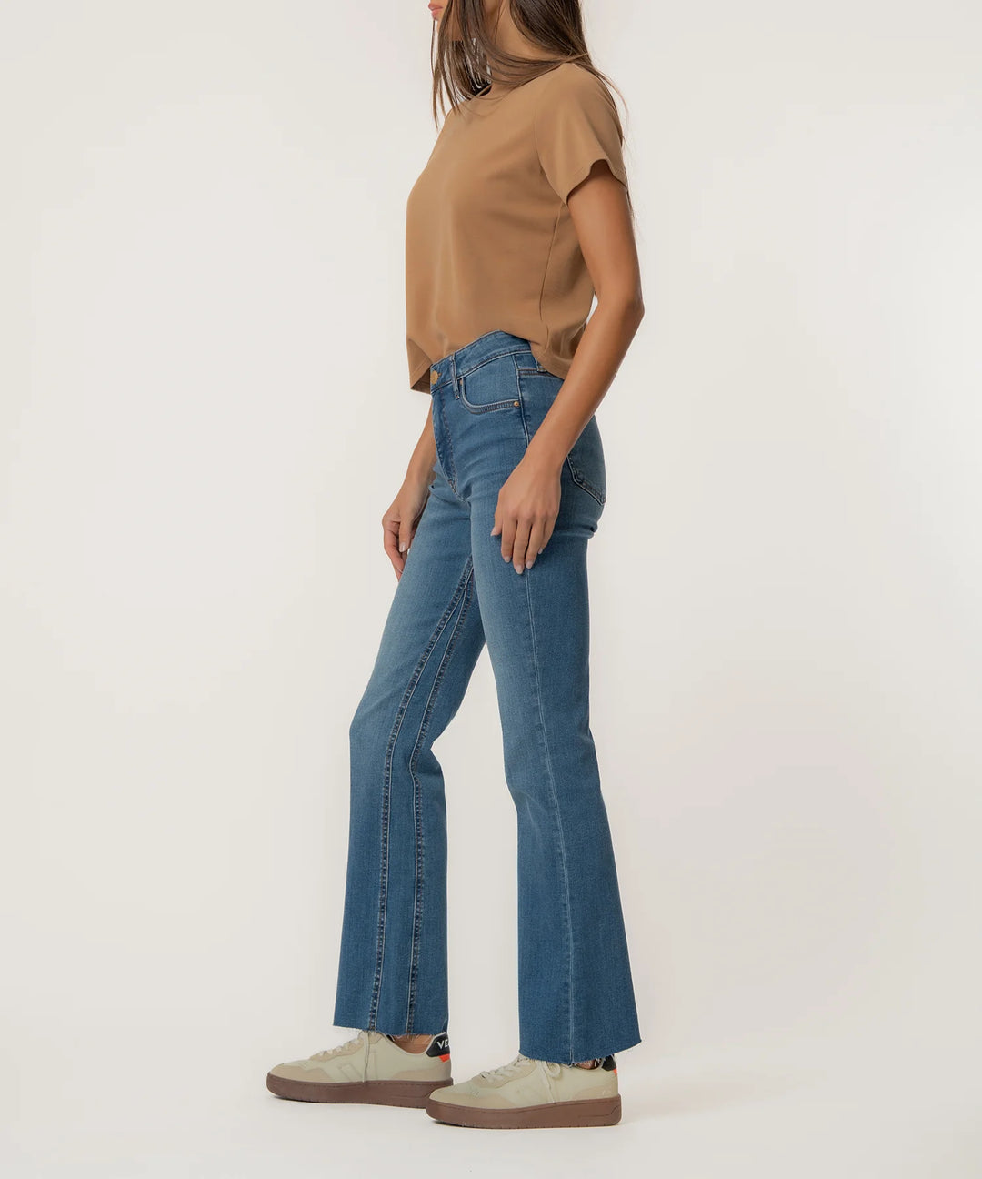 Person wearing blue flared jeans and a brown top on a white background