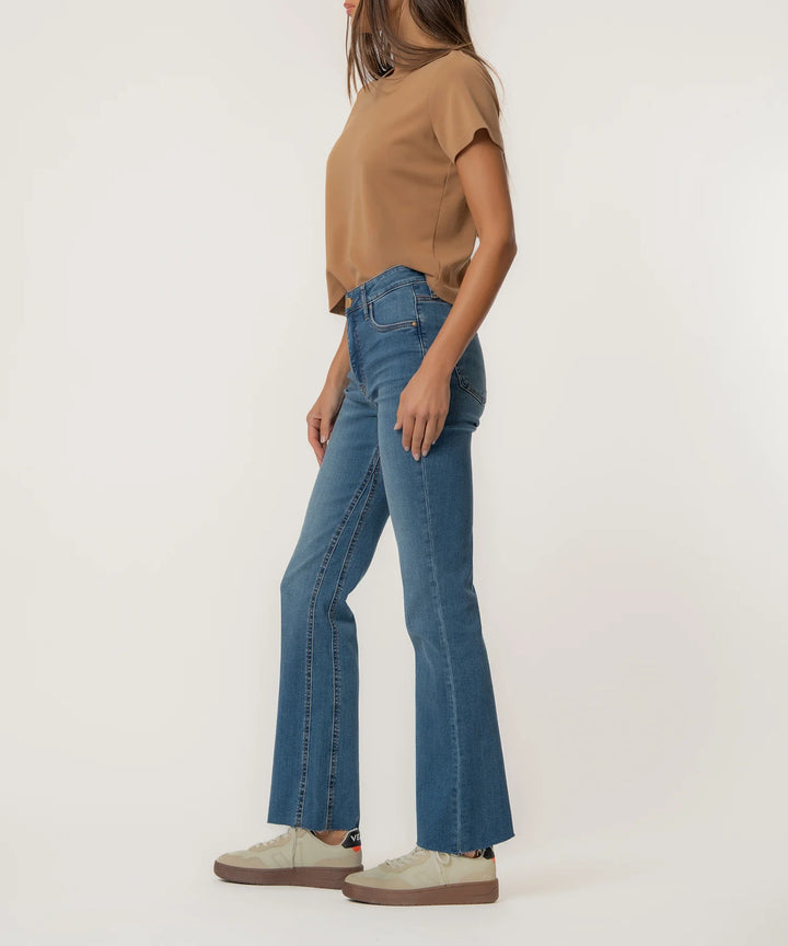 Person wearing blue flared jeans and a brown top on a white background