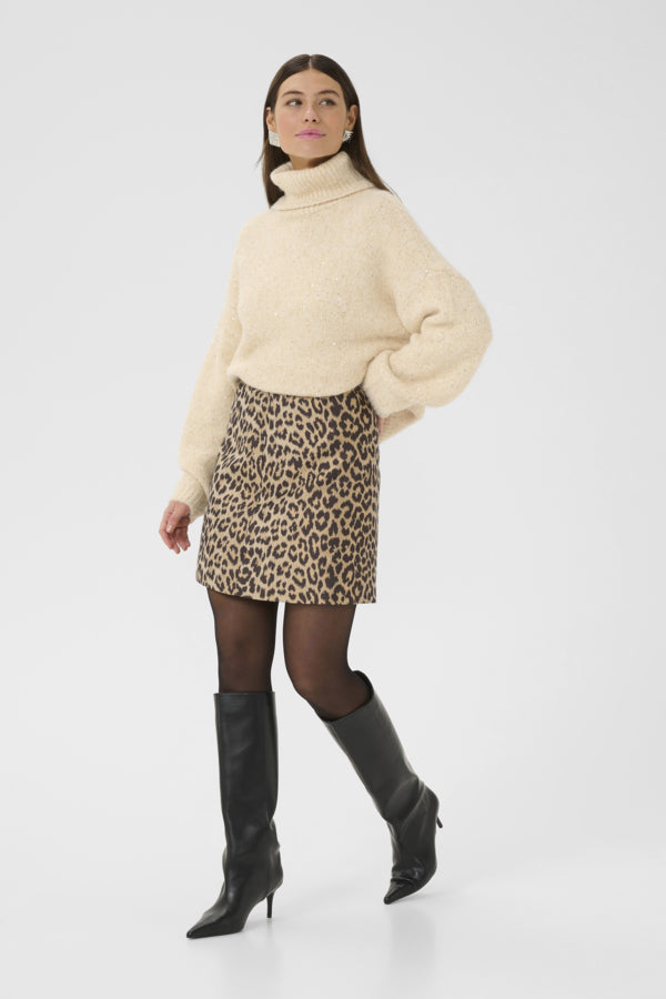 Woman wearing a cream sweater, leopard print skirt, and black knee-high boots on a white background