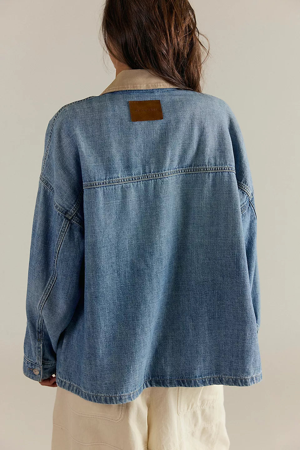 Person wearing a blue denim jacket with a beige patch on a plain background