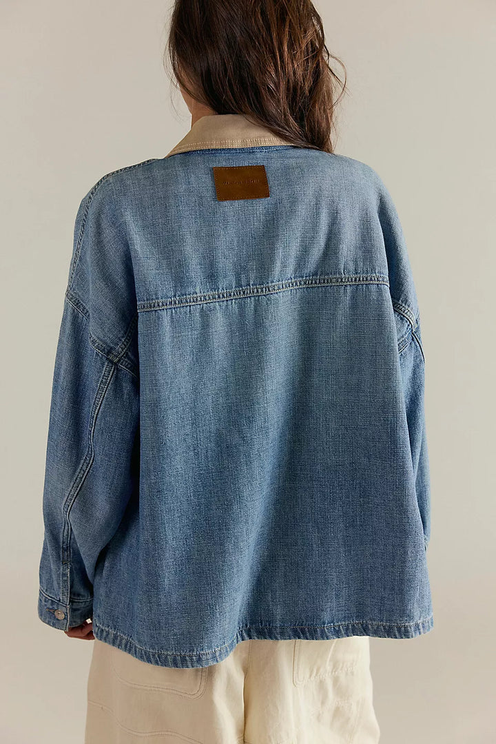 Person wearing a blue denim jacket with a beige patch on a plain background